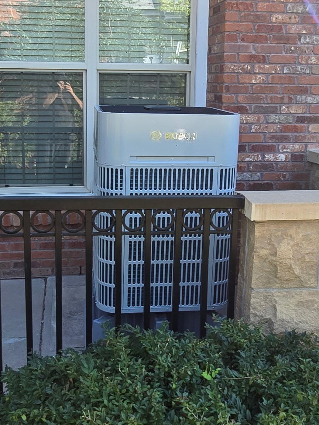Heat pump installation: Bosch outdoor heat pump unit set on a pad alongside a brick home